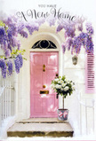 This photograph shows a storybook-style doorway in Queensbury that has been transformed into a floral welcome, ideal for celebrating a new home or milestone move. The front door is painted in a soft, candy-floss pink, subtly glowing as though touched by the last rays of afternoon sun drifting over from nearby Queensbury Park. Flanking and arching above it, trailing wisteria in delicate shades of lavender cascades down, each raceme of blossom hanging loosely to frame the doorway in a fragrant curtain. The surrounding wall is a clean, warm white, lightly textured, creating a gentle contrast that lets the pastel colours sing. Resting directly at the threshold is a stylish grey bucket, the kind a careful florist would choose for its understated elegance, filled generously with white and cream roses. The roses are full and plush, some blooms more open than others, giving a natural, freshly arranged feel, while tendrils of soft green foliage weave among them. Around the base of the bucket, a blush-pink ribbon has been tied in a simple yet graceful bow, echoing the tone of the door and reinforcing the romantic, harmonious colour palette. The overall mood is calm, hopeful, and quietly joyful, like arriving at a new address off Turner Road with boxes still to unpack but flowers already making the space feel lived in. This arrangement feels perfectly suited to a Queensbury housewarming or congratulations gift, capturing the emotions of anticipation, comfort, and the simple happiness of being welcomed home by flowers.