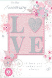 This image presents a romantic anniversary card that blends gentle pastel pinks with silvery greys to create an atmosphere of treasured intimacy, as if capturing the quiet warmth of a long, shared life in Queensbury. The focal point is the word "LOVE," spelled out in soft, raised glitter letters; each stroke looks slightly cushioned and tactile, with the glitter giving off a refined, silvery shimmer. The letter "O" is replaced by a sparkling heart, textured in denser silver glitter that stands out more boldly, like a small piece of jewellery nestled at the centre of the design. Around this, delicate illustrated blooms unfold with a watercolour softness, their petals in shades of blush, mauve, and pale rose, gently outlined in fine grey lines. The flowers are interlaced with slender vines and curling tendrils, echoing the relaxed curves of stems in an English spring garden or a hand-tied arrangement prepared by a Queensbury florist. Tiny details-scattered petals, subtle swirls, and discreet butterfly shapes-add a sense of motion and lightness, as though the decoration is drifting lightly across the card. The background is a soft pink wash that deepens slightly at the edges, enhancing the central heart and lettering. Along the top or side, the phrase "On Our Anniversary" appears in an understated script, while "I love you today and always" sits lower down, also in graceful, flowing type. Together, the layout and colours convey a gentle sense of occasion: a keepsake card as tender as a whispered promise, well suited to accompany an anniversary bouquet delivered to a quiet home on a residential street in Queensbury.